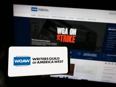 Stuttgart, Almanya - 08-26-2023: Web sitesi önünde ekranda, üzerinde İşçi Sendikası Yazarları Derneği (WGAW) logosu olan akıllı telefon tutan kişi. Telefon ekranına odaklan.