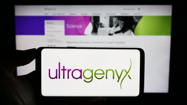 Stuttgart, Almanya - 08-26-2023: ABD 'li Ultragenyx Pharmaceutical Inc. şirketinin logosuyla cep telefonu sahibi kişi iş sayfasının önünde ekranda. Telefon ekranına odaklan.