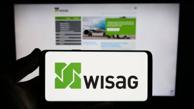 Stuttgart, Germany - 08-28-2023: Person holding smartphone with logo of German company WISAG Dienstleistungsholding SE on screen in front of website. Focus on phone display. clipart