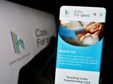 Stuttgart, Almanya - 08-28-2023: Malezyalı sağlık şirketi IHH Healthcare Berhad 'ın internet sayfası logolu cep telefonu tutan kişi. Telefon ekranının merkezine odaklan.
