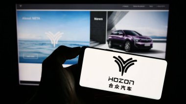 Stuttgart, Almanya - 08-28-2023: Hozon Auto New Energy Co. Ltd. 'nin logosuyla cep telefonu sahibi kişi iş sayfasının önünde ekranda. Telefon ekranına odaklan.