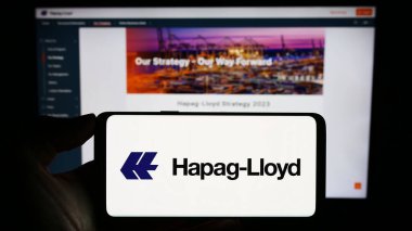 Stuttgart, Germany - 08-28-2023: Person holding cellphone with logo of German shipping company Hapag-Lloyd AG on screen in front of business webpage. Focus on phone display. clipart