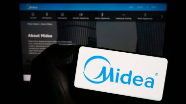 Stuttgart, Almanya - 08-28-2023: Çinli ev aletleri şirketi Midea Group 'un logosunu elinde tutan kişi web sitesinin önünde ekranda. Telefon ekranına odaklan.