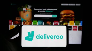 Stuttgart, Almanya - 08-28-2023: Gıda dağıtım şirketi Deliveroo Holding 'in logosuna sahip akıllı telefon sahibi kişi web sitesinin önünde ekranda. Telefon ekranına odaklan.