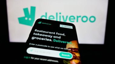 Stuttgart, Almanya - 08-28-2023: Gıda dağıtım şirketi Deliveroo Holding 'in web sitesiyle birlikte cep telefonu, iş logosu önünde ekranda. Telefon ekranının sol üst kısmına odaklan.