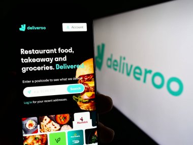 Stuttgart, Almanya - 08-28-2023: Gıda dağıtım şirketi Deliveroo Holding 'in internet sayfası ile cep telefonu tutan kişi logo ile ekranda. Telefon ekranının merkezine odaklan.