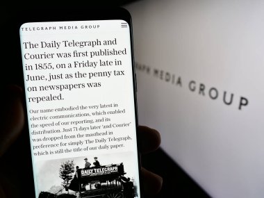 Stuttgart, Almanya - 08-28-2023: Telegraph Media Group Limited (TMG) şirketinin web sayfası ile cep telefonu tutan kişi logolu ekranda. Telefon ekranının merkezine odaklan.