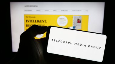 Stuttgart, Almanya - 08-28-2023: İş sayfası önünde ekranda Telegraph Media Group Limited (TMG) şirketinin logosuyla cep telefonu tutan kişi. Telefon ekranına odaklan.