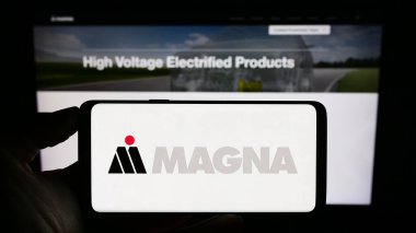 Stuttgart, Almanya - 08-29-2023: Otomotiv şirketi Magna International Inc. 'in logosuyla cep telefonu sahibi kişi iş sayfasının önünde ekranda. Telefon ekranına odaklan.