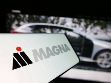 Stuttgart, Germany - 08-29-2023: Mobile phone with logo of automotive company Magna International Inc. on screen in front of business website. Focus on left of phone display. clipart