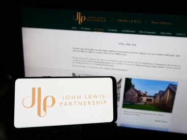 Stuttgart, Almanya - 08-29-2023: Perakende şirketi John Lewis Partnership plc 'in logosuna sahip akıllı telefon sahibi kişi web sitesinin önünde ekranda. Telefon ekranına odaklan.