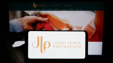 Stuttgart, Almanya - 08-29-2023: Perakende şirketi John Lewis Partnership plc 'in logosuyla cep telefonu sahibi kişi iş sayfasının önünde ekranda. Telefon ekranına odaklan.