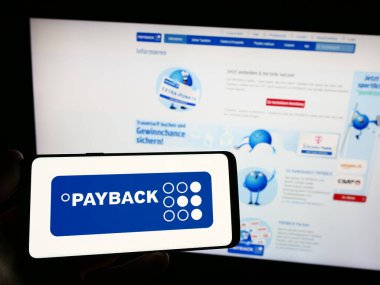 Stuttgart, Germany - 09-01-2023: Person holding smartphone with logo of German loyalty management company Payback GmbH on screen in front of website. Focus on phone display. clipart