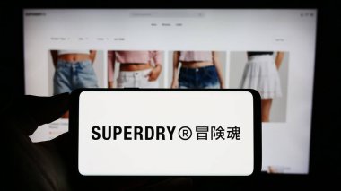Stuttgart, Almanya - 09-01-2023: İngiliz giyim şirketi Superdry plc 'in logosunun bulunduğu cep telefonu sahibi kişi iş sayfasının önünde ekranda. Telefon ekranına odaklan.