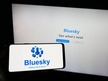 Stuttgart, Germany - 09-02-2023: Person holding smartphone with logo of social network initiative Bluesky on screen in front of website. Focus on phone display. clipart