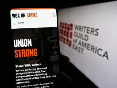 Stuttgart, Almanya - 09-02-2023: Doğu Amerika İşçi Sendikası Yazarları Sendikası (WGAE) sitesi ile akıllı telefon sahibi kişi ekranda logolu. Telefon ekranının merkezine odaklan.