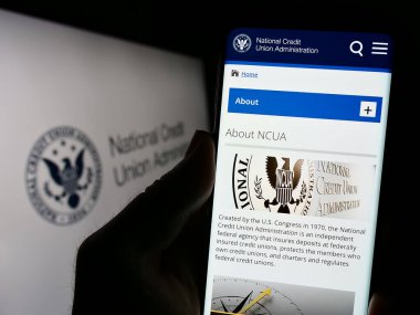 Stuttgart, Almanya - 09-02-2023: Ulusal Kredi Birliği İdaresi 'nin (NCUA) web sitesi ile cep telefonu elinde tutan kişi, mühür önünde ekranda. Telefon ekranının merkezine odaklan.