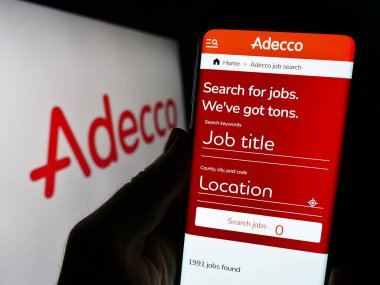 Stuttgart, Almanya - 09-02-2023: Personel alma şirketi Adecco 'nun internet sayfası olan cep telefonu, iş logosu önünde ekranda. Telefon ekranının merkezine odaklan.