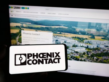 Stuttgart, Germany - 09-02-2023: Person holding smartphone with logo of German company Phoenix Contact GmbH Co. KG on screen in front of website. Focus on phone display. clipart