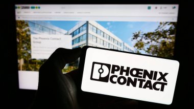 Stuttgart, Germany - 09-02-2023: Person holding mobile phone with logo of German company Phoenix Contact GmbH Co. KG on screen in front of web page. Focus on phone display. clipart