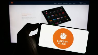 Stuttgart, Almanya - 09-02-2023: Telekomünikasyon şirketi Liberty Global 'in logosuna sahip akıllı telefon sahibi kişi web sitesinin önünde ekranda. Telefon ekranına odaklan.