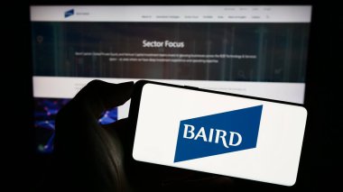 Stuttgart, Germany - 09-06-2023: Person holding cellphone with logo of US investment company Baird Capital on screen in front of business webpage. Focus on phone display. clipart