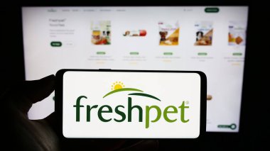 Stuttgart, Germany - 09-06-2023: Person holding cellphone with logo of US pet food company Freshpet Inc. on screen in front of business webpage. Focus on phone display. clipart