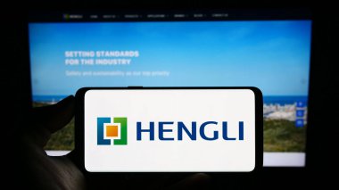 Stuttgart, Almanya - 09-06-2023: Çinli petrokimya şirketi Hengli Group 'un logosuyla cep telefonu sahibi kişi iş sayfasının önünde ekranda. Telefon ekranına odaklan.