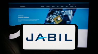 Stuttgart, Germany - 09-08-2023: Person holding smartphone with logo of US electronics company Jabil Inc. on screen in front of website. Focus on phone display. clipart