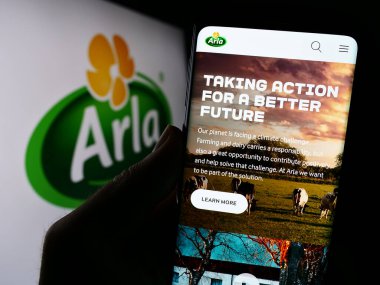 Stuttgart, Almanya - 09-08-2023: İskandinav süt ürünleri şirketi Arla Foods amba 'nın web sayfası ile logo önünde cep telefonu tutan kişi. Telefon ekranının merkezine odaklan.