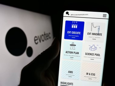 Stuttgart, Almanya - 09-09-2023: Alman ilaç keşif şirketi Evotec SE 'nin internet sitesi ile cep telefonu tutan kişi logonun önünde ekranda. Telefon ekranının merkezine odaklan.