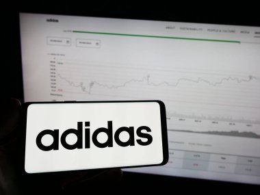 Stuttgart, Almanya - 09-09-2023: Alman giyim ve ayakkabı firması Adidas AG 'nin logosu olan cep telefonu sahibi kişi web sayfasının önünde ekranda. Telefon ekranına odaklan.