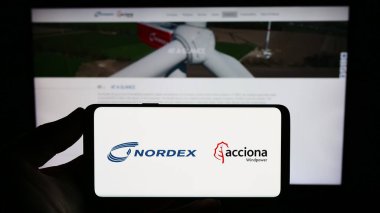 Stuttgart, Germany - 09-10-2023: Person holding smartphone with logo of German wind turbine company Nordex SE on screen in front of website. Focus on phone display. clipart