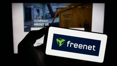 Stuttgart, Germany - 09-10-2023: Person holding smartphone with logo of German telecommunications company Freenet AG on screen in front of website. Focus on phone display. clipart