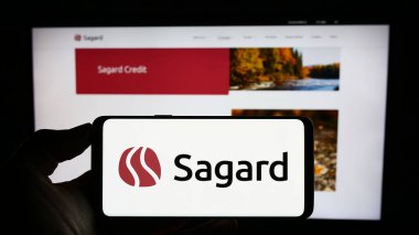 Stuttgart, Almanya - 07-26-2023: Kanadalı yatırım şirketi Sagard 'ın logosuyla cep telefonu sahibi kişi iş sayfasının önünde ekranda. Telefon ekranına odaklan.