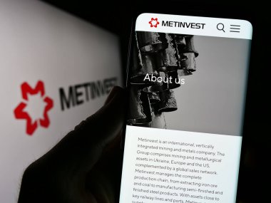 Stuttgart, Almanya - 07-27-2023: Çelik şirketi Ukraynalı Metinvest Holding LLC 'nin web sitesi ile cep telefonu tutan kişi logolu ekranda. Telefon ekranının merkezine odaklan.