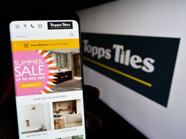 Stuttgart, Almanya - 07-27-2023: İngiliz perakende şirketi Topps Tiles plc 'in web sayfası ile akıllı telefon sahibi kişi logonun önünde ekranda. Telefon ekranının merkezine odaklan.