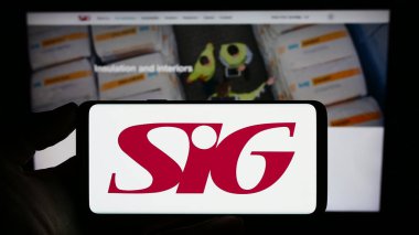 Stuttgart, Germany - 07-27-2023: Person holding smartphone with logo of British building materials company SIG plc on screen in front of website. Focus on phone display. clipart