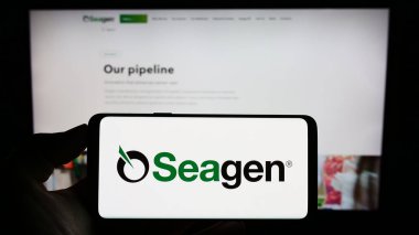 Stuttgart, Almanya - 07-28-2023: ABD 'li biyoteknoloji şirketi Seagen Inc.' nin logosunun bulunduğu cep telefonu sahibi kişi iş sayfasının önünde ekranda. Telefon ekranına odaklan.