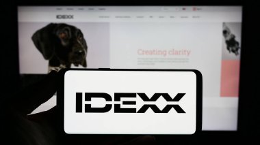 Stuttgart, Almanya - 07-29-2023: İnternet sitesi önünde üzerinde ABD veteriner firması IDEXX Laboratories Inc. 'in logosu bulunan akıllı telefon sahibi kişi. Telefon ekranına odaklan.