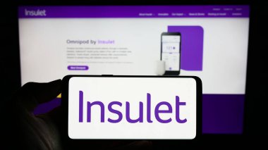 Stuttgart, Germany - 07-29-2023: Person holding smartphone with logo of US medical device company Insulet Corporation on screen in front of website. Focus on phone display. clipart