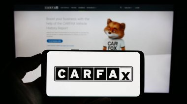 Stuttgart, Germany - 07-29-2023: Person holding mobile phone with logo of American vehicle data company CARFAX Inc. on screen in front of business webpage. Focus on phone display. clipart