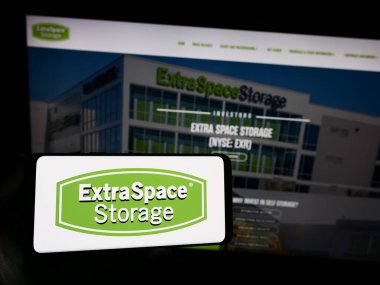 Stuttgart, Germany - 07-29-2023: Person holding smartphone with logo of US company Extra Space Storage Inc. on screen in front of website. Focus on phone display. clipart