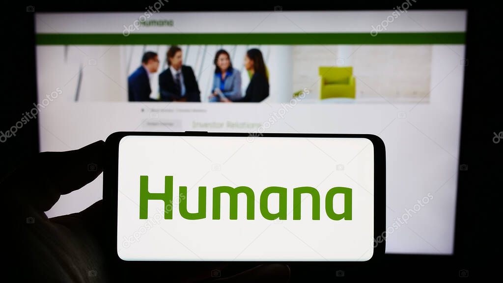 Stuttgart, Germany - 07-28-2023: Person holding mobile phone with logo of American health insurance company Humana Inc. on screen in front of web page. Focus on phone display.
