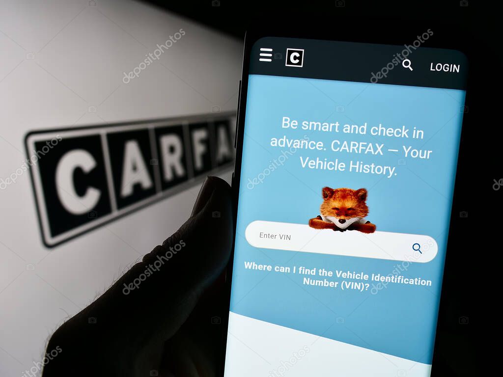 Stuttgart, Germany - 07-29-2023: Person holding cellphone with webpage of US vehicle data company CARFAX Inc. on screen in front of logo. Focus on center of phone display.