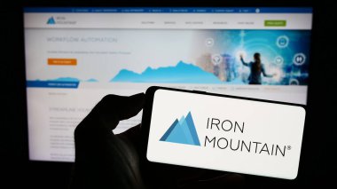 Stuttgart, Almanya - 07-29-2023: ABD 'li Iron Mountain Inc. şirketinin logosuyla cep telefonu sahibi kişi iş sayfasının önünde ekranda. Telefon ekranına odaklan.