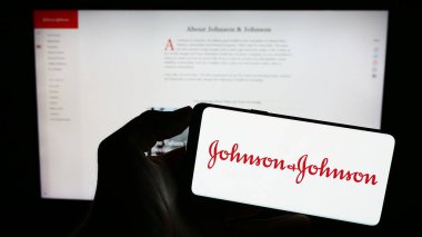 Stuttgart, Almanya - 07-29-2023: ABD 'li Johnson ve Johnson (JNJ) şirketinin logosuyla cep telefonu sahibi kişi iş sayfası önünde ekranda. Telefon ekranına odaklan.
