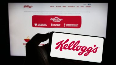 Stuttgart, Almanya - 07-29-2023: ABD 'li şirket The Kellog Company' nin (Kellogg 's) logosunun logosunu elinde tutan kişi web sitesinin önünde ekranda. Telefon ekranına odaklan.