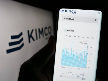 Stuttgart, Almanya - 07-30-2023: ABD 'li emlak şirketi Kimco Realty Corporation' ın logolu web sayfası ile akıllı telefon tutan kişi. Telefon ekranının merkezine odaklan.