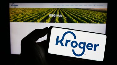 Stuttgart, Almanya - 07-30-2023: Amerikan perakende şirketi logosu olan cep telefonu sahibi kişi Kroger Şirketi web sayfasının önünde ekranda. Telefon ekranına odaklan.